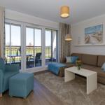 Wohnzimmer mit Sofa, Sessel und Balkonansicht.
