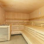 Sauna mit Holzbanken und Ofen, Wanduhr und Deckenleuchte sichtbar.