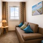 Ein Sofa mit Kissen, Fenster mit Jalousie und Wandbild.