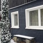 Schneebedeckter Holzausbau mit Fenstern und Bank im Vordergrund.