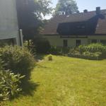 Grüner Garten mit Rasenfläche und Beeten vor einem Haus mit dunklem Dach.