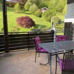 Terrasse mit Tisch, Stühlen und Grill. Blick auf grünen Garten und Wald.