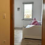 Schlafzimmer mit weißem Bett, Holzboden und Fenster mit Hundenbild.