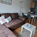 Wohnzimmer mit Sofa, Esstisch und Küchenbereich. Holzboden und Wandbild mit Meeresmotiven.