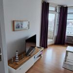 Wohnzimmer mit Holzboden, TV-Möbel und Balkontür mit lila Vorhängen.