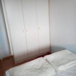 Schlafzimmer mit Bett und weißen Kleidern. Hinter dem Bett steht ein großer Schrank.