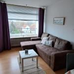 Wohnzimmer mit braunem Sofa, Tisch und Fenster mit Blick auf die Straße.