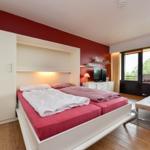 Schlafzimmer mit Bett, Fernseher und Balkonansicht.