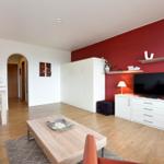 Wohnzimmer mit roter Wand, TV, Schrank und Holzboden.