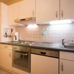 Kitchen with worktop, sink, stove, oven, cabinets, and wall tiles.