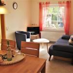 Living room with sofa, armchair, table, and TV. Window with red curtains. Table with wine and flowers.