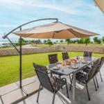 Terrasse mit Tisch, Stühlen und Sonnenschirm. Blick auf Grasfläche und Wasser.