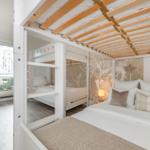 Schlafzimmer mit Doppelbett und Doppelstockbetten, Holzdecke und Fenster mit Vorhang.