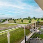 Balcony with table, chairs, and wine overlooking green park and water.