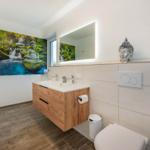 Badezimmer mit Holzwaschtisch, Spiegel und Buddha-Dekoration an der Wand.