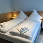 Doppelbett mit weißen Laken und Handtüchern, Holzpaneelen und Wandlampen.