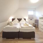 Zimmer mit Doppelbett, Schrank und Fenster. Holzboden und weiße Wände.