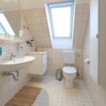 Badezimmer mit Waschbecken, Toilette und Dachfenster. Fliesenwand und Holzmatte.