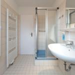 Badezimmer mit Dusche, Waschbecken und Heizkörper an der Wand.