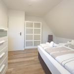 Zimmer mit Doppelbett, Schrank und Holzboden. Dachschräge und Fenster sichtbar.