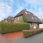 Haus mit braunem Dach und grüner Hecke vor einem weißen Zaun.