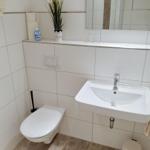 Badezimmer mit Waschbecken, Spiegel, Toilette und Handtuchhalter.