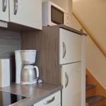 Küche mit Kaffeemaschine, Mikrowelle und Kühlschrank. Treppe mit Holzgeländer rechts.