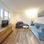 Wohnzimmer mit blauem Sofa, Holzboden und Fernseher auf Schrank