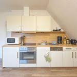 Küche mit weißen Schränken, Holz Arbeitsplatte und Edelstahl Geräten unter schrägem Dach