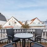 Terrasse mit Tisch und Stühlen. Blick auf Gebäude und Restaurant Mai.