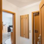 Flur mit Holztüren, Kleiderhaken und Sicht auf Wohn- und Arbeitszimmer.