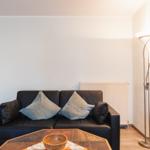 Schwarzes Sofa mit Kissen, Tisch und Stehlampe im Wohnzimmer.