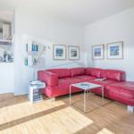 Ein Wohnzimmer mit rotem Sofa, Glas-Tisch und Holzboden. An der Wand hängen Bilder.