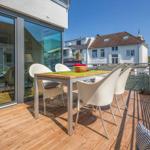 Terrasse mit Tisch und Stühlen, Holzboden, Blick auf Gebäude.