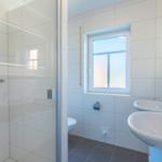 Badezimmer mit Dusche, zwei Waschbecken und Fenster.