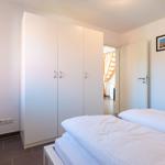 Schlafzimmer mit weißem Bett, Kleiderschrank und Fenster mit Pflanze.