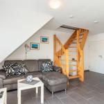 Wohnzimmer mit Sofa, Tisch und Holztreppe zur oberen Etage.