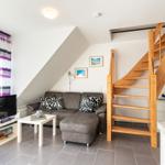 Wohnzimmer mit Sofa, Fernseher und Holztreppe zur oberen Etage.