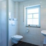 Badezimmer mit Toilette, Waschbecken und Dusche. Fenster mit Blick nach draußen.
