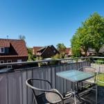 Terrasse mit Tisch und Stühlen. Blick auf Wohnhäuser und Bäume unter blauem Himmel.