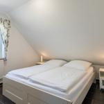 Doppelbett mit weißen Laken, zwei Nachttische mit Lampen und Fenster mit Vorhängen.