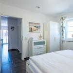 Schlafzimmer mit weißem Bett, Kleiderschrank und Fenster mit Vorhängen.