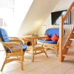 Wohnbereich mit Rattanmöbeln, TV und Treppe zur oberen Etage.