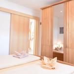 Schlafzimmer mit Bett, Holzschrank und Schlupftür. Handtuch als Vogel dekoriert.