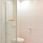 Bad mit Dusche, Toilette und Waschbecken. Handtuch auf Regal.