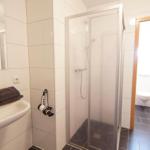 Badezimmer mit Dusche, Waschbecken und Toilette. Fliesenboden und Spiegel.