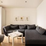 Ein Wohnzimmer mit grauem Sofa, weißem Tisch und weißen Wänden.
