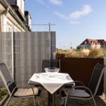 Terrasse mit Tisch und zwei Stühlen, umgeben von Zaun und Pflanzen.