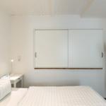 Schlafzimmer mit Bett, Nachttisch, Schrank und Staubsauger an der Wand.