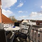 Terrasse mit Tisch und Stühlen, Blick auf Dächer und Himmel.